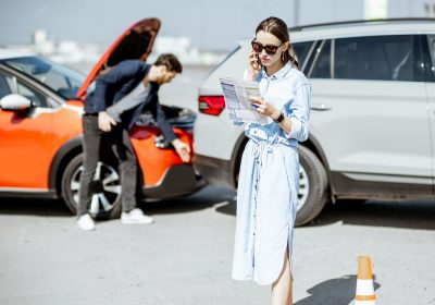 Woman calling road assistance or insurance company standing on the road after the car collision, man checking the damage